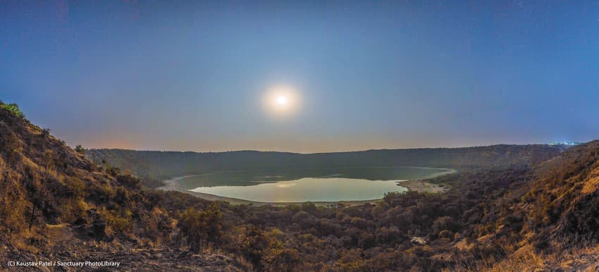 The moon sparkles in the night sky as it lights up the Lonar crater below. The impact crater was formed around 50,000 years ago when a meteor hit the earth. Today, it cradles a lake at the center and a dense forest along the rim.